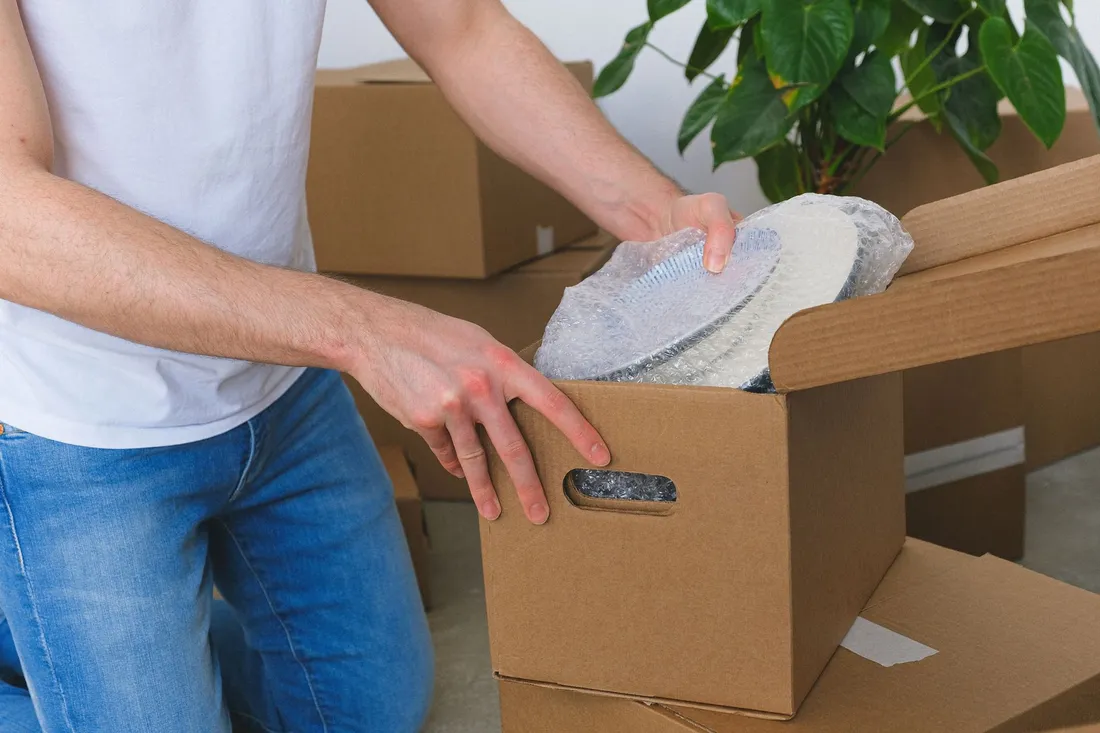 Geschirr wird in Packpapier gewickelt und in einen Umzugskarton gepackt