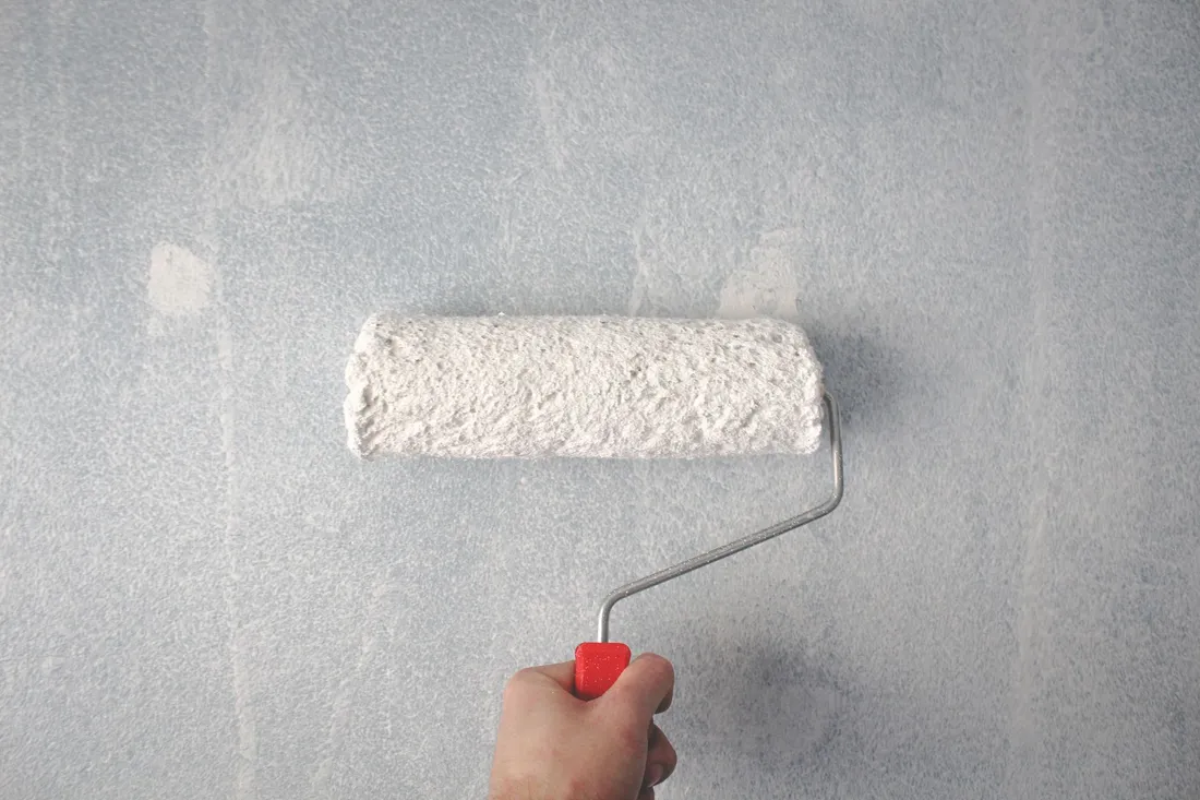 Maler streicht eine Wand mit der Rolle in einer leeren Wohnung